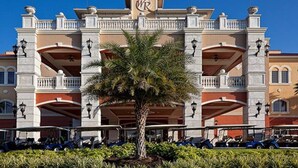 Ein mehrstöckiges Hotel mit zentralem Eingang, Balkonen und einer Palme im Vordergrund.