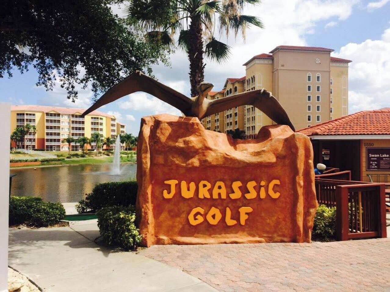 Skilt for Jurassic Golf med en palmetræ og en bygning i baggrunden.