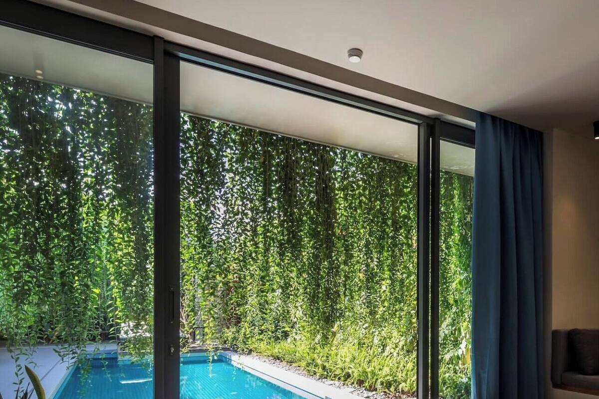 A bedroom with a large window overlooking a swimming pool and lush greenery.