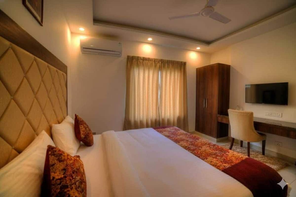 A hotel room with a large bed, a desk, a chair, a television, and a ceiling fan.