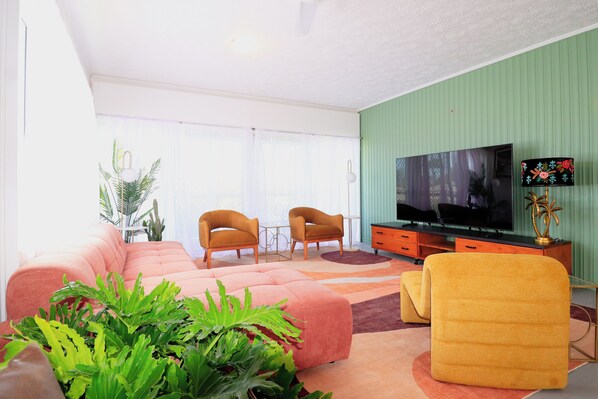 A living room with a sofa, two armchairs, a television, and a plant.