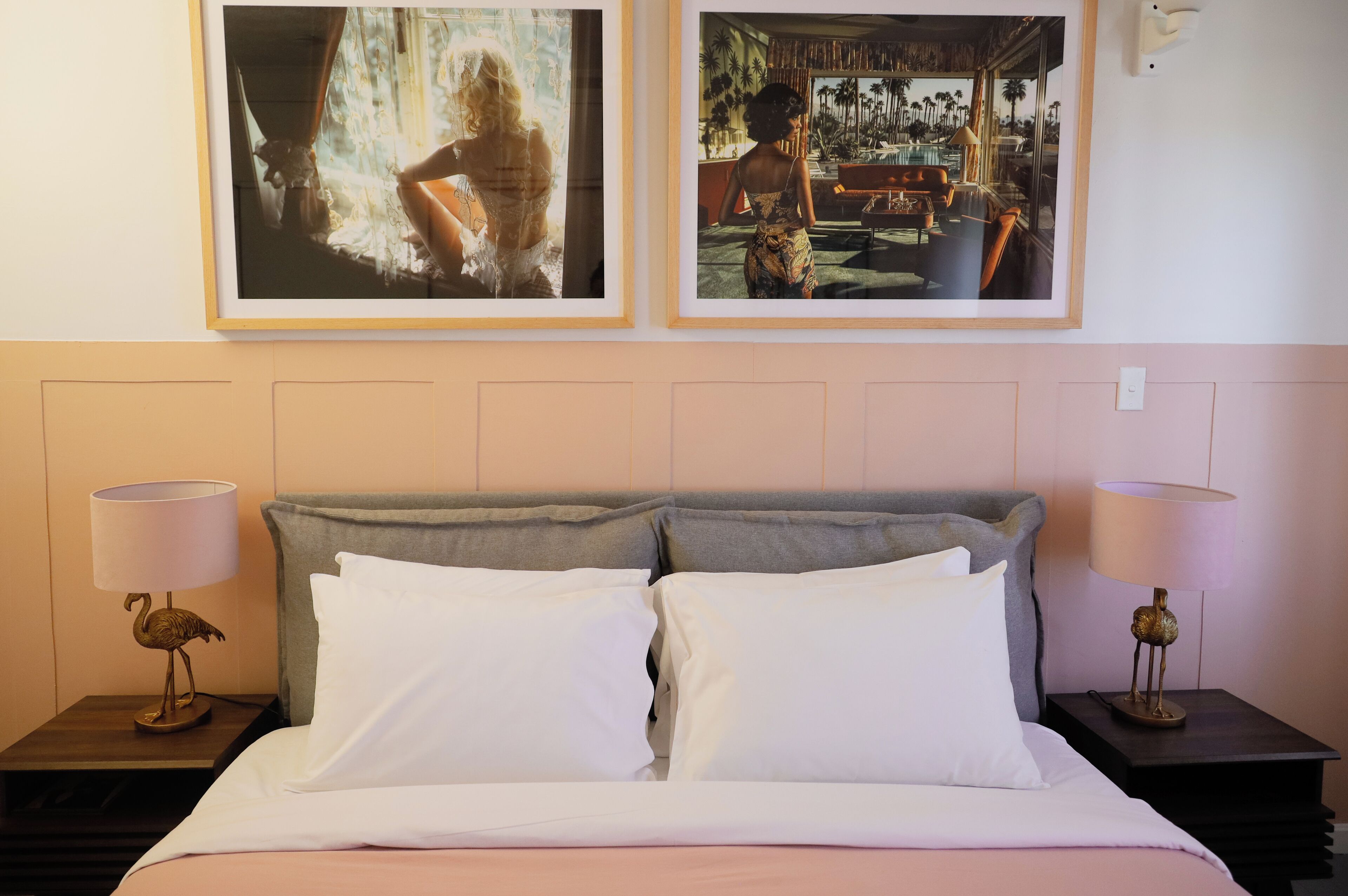 Un lit bien fait, avec du linge de lit blanc, deux tableaux encadrés au-dessus, et deux tables de chevet avec des lampes.