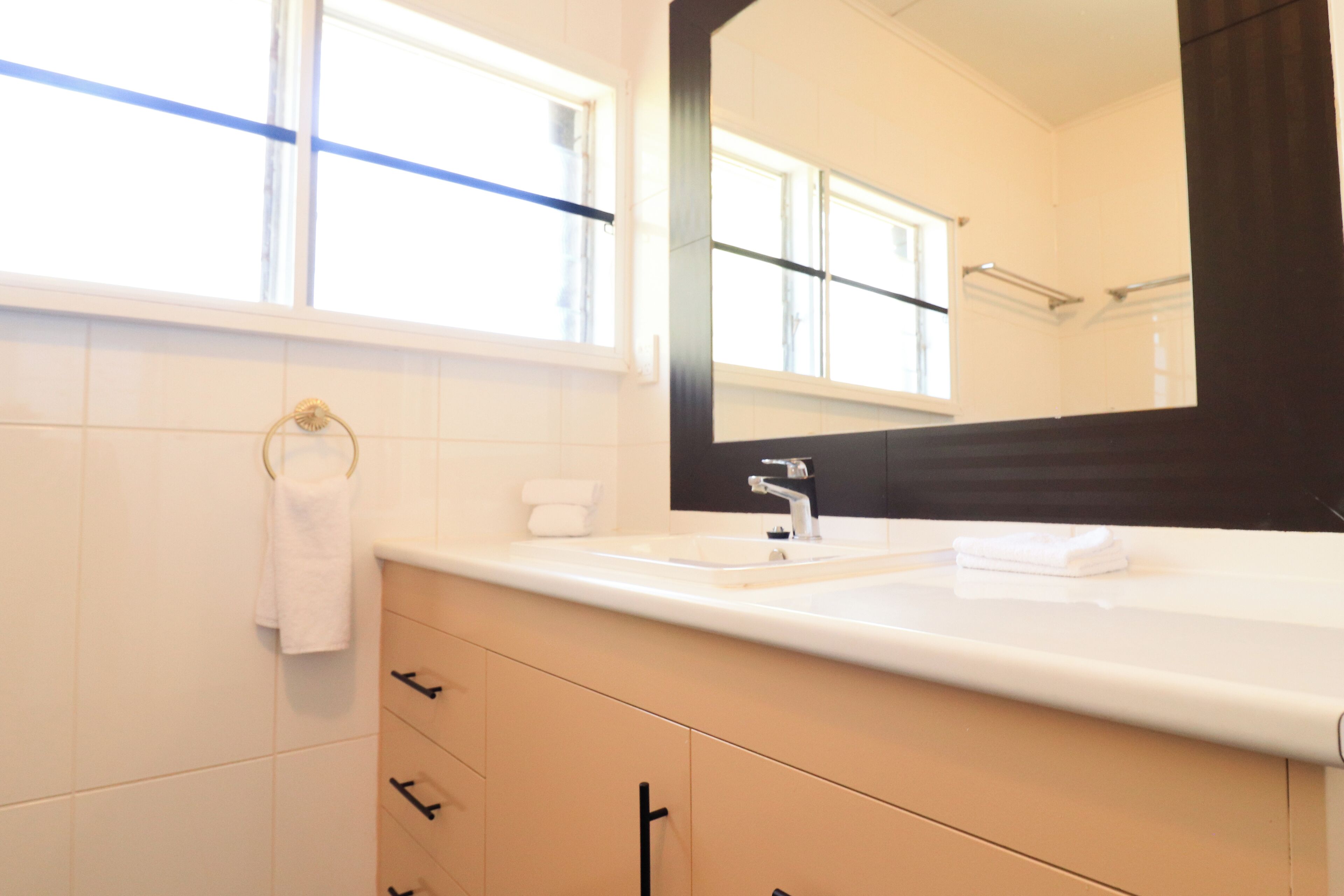 A modern bathroom with a white sink, a large mirror, and a window with blinds.