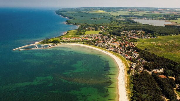 Una vista aerea di una cittadina costiera con spiaggia, zone residenziali e un porto turistico.
