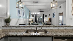 A kitchen with granite countertops, a double sink, pendant lights, and a dining area in the background. - Designer-Renovated Condo in a Gorgeous Tropical Oasis! (Davenport)