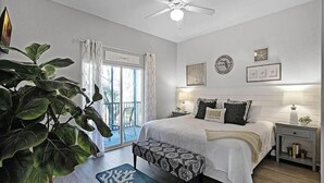 A bedroom with a bed, bedside tables, a ceiling fan, a large window with curtains, and a potted plant. - Designer-Renovated Condo in a Gorgeous Tropical Oasis! (Davenport)