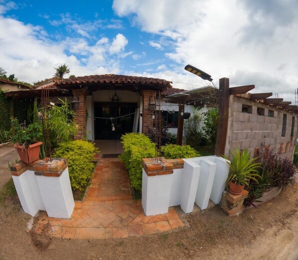 A house with a tiled roof, a brick entrance, and a garden with potted plants.