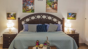 A bedroom with a wooden headboard, a bed with patterned pillows, two bedside tables with lamps, and wall art depicting landscapes. - Casa San Isidro is a sparkling clean, and family friendly house (Copán Ruinas)