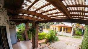 A covered patio area with a brick floor, a small garden, and a yellow building in the background. - Casa San Isidro is a sparkling clean, and family friendly house (Copán Ruinas)