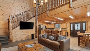 Interno di una baita di legno con una scala in legno, un soggiorno con divano in pelle, zona pranzo e cucina.
