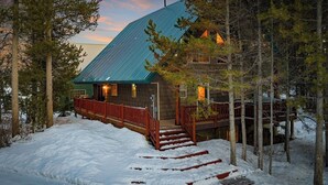 Una baita con tetto ripido, veranda in legno e terreno innevato.