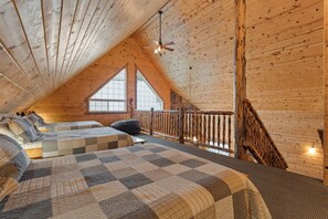 Une chambre confortable située sous les toits, avec deux lits, un plafond en bois et une vue sur l’extérieur grâce à de grandes fenêtres.