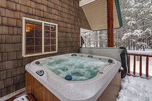 Un bain à remous sur une terrasse en bois, avec vue sur des arbres couverts de neige.