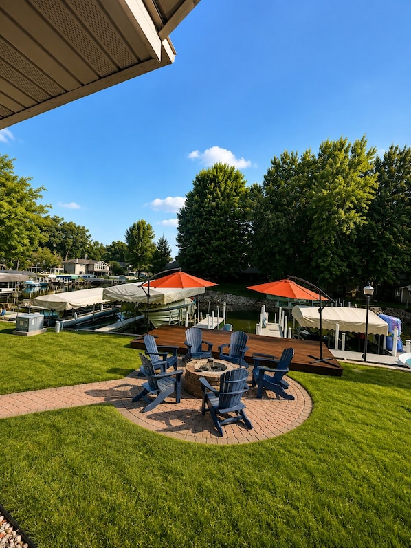 Eine Terrasse mit Sitzgelegenheiten im Freien, einer Feuerstelle und Blick auf einen See mit Booten.