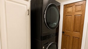 A laundry room with stacked washers and dryers, a wooden door, and white cabinetry. - Waterfront Arnolds Park 4BR Dock, Boat Slip, Kayaks & Paddleboards (Arnolds Park)