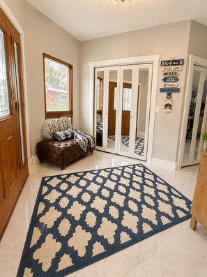 A hallway with a patterned rug, a brown leather bench, and a door leading to a room with a view of a house. - Okoboji Waterfront 5BR• Private Dock, Boat Slip, Kayaks & Paddleboards (Arnolds Park)