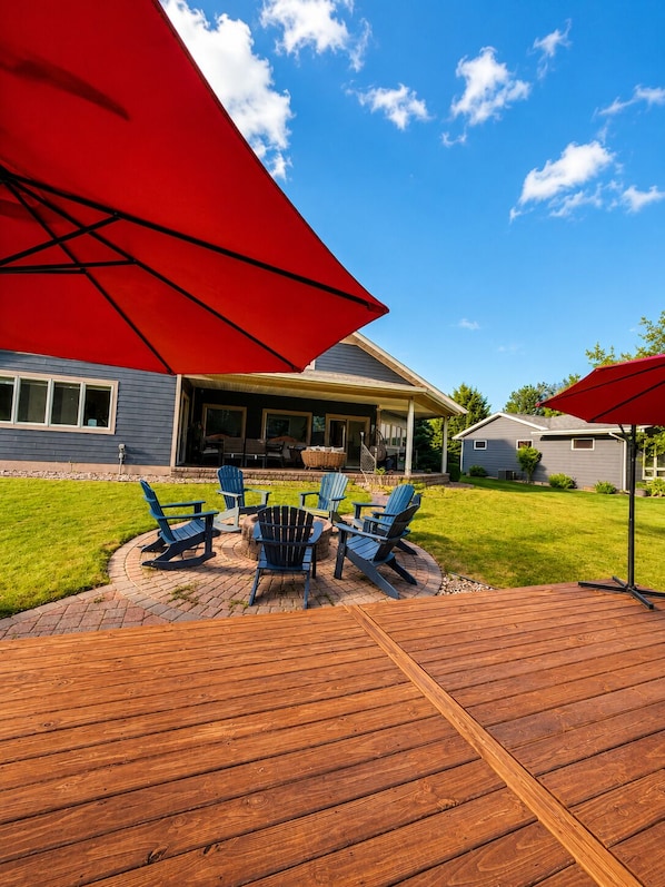 A patio with Adirondack chairs and a fire pit, a covered area with a grill, and a wooden deck. - Okoboji Waterfront 5BR• Private Dock, Boat Slip, Kayaks & Paddleboards (Arnolds Park)