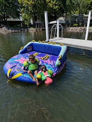 Ein aufblasbarer Pool mit zwei Kindern und einem Hund, umgeben von einer Anlegestelle und Häusern.