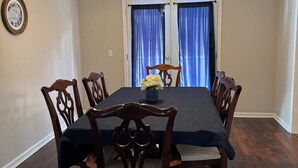 Comedor con una mesa y sillas de madera oscura, ventilador de techo y ventana con cortinas azules.