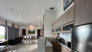 A modern kitchen with a stainless steel refrigerator, marble countertops, and a dining area with a black leather sofa and a dining table. - Anemos Resort By Tamastu (Cijeruk)
