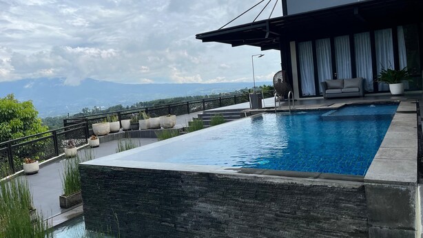 A rooftop infinity pool with a view of mountains, a modern outdoor seating area, and a large potted plant. - Anemos Resort By Tamastu (Cijeruk)