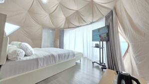 A modern bedroom with a large bed, a TV, and a kettle on a wooden table. - Anemos Resort By Tamastu (Cijeruk)