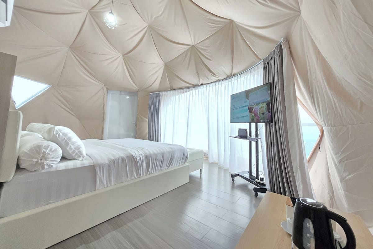 Une chambre moderne avec un grand lit, une télévision et une bouilloire posée sur une table en bois.