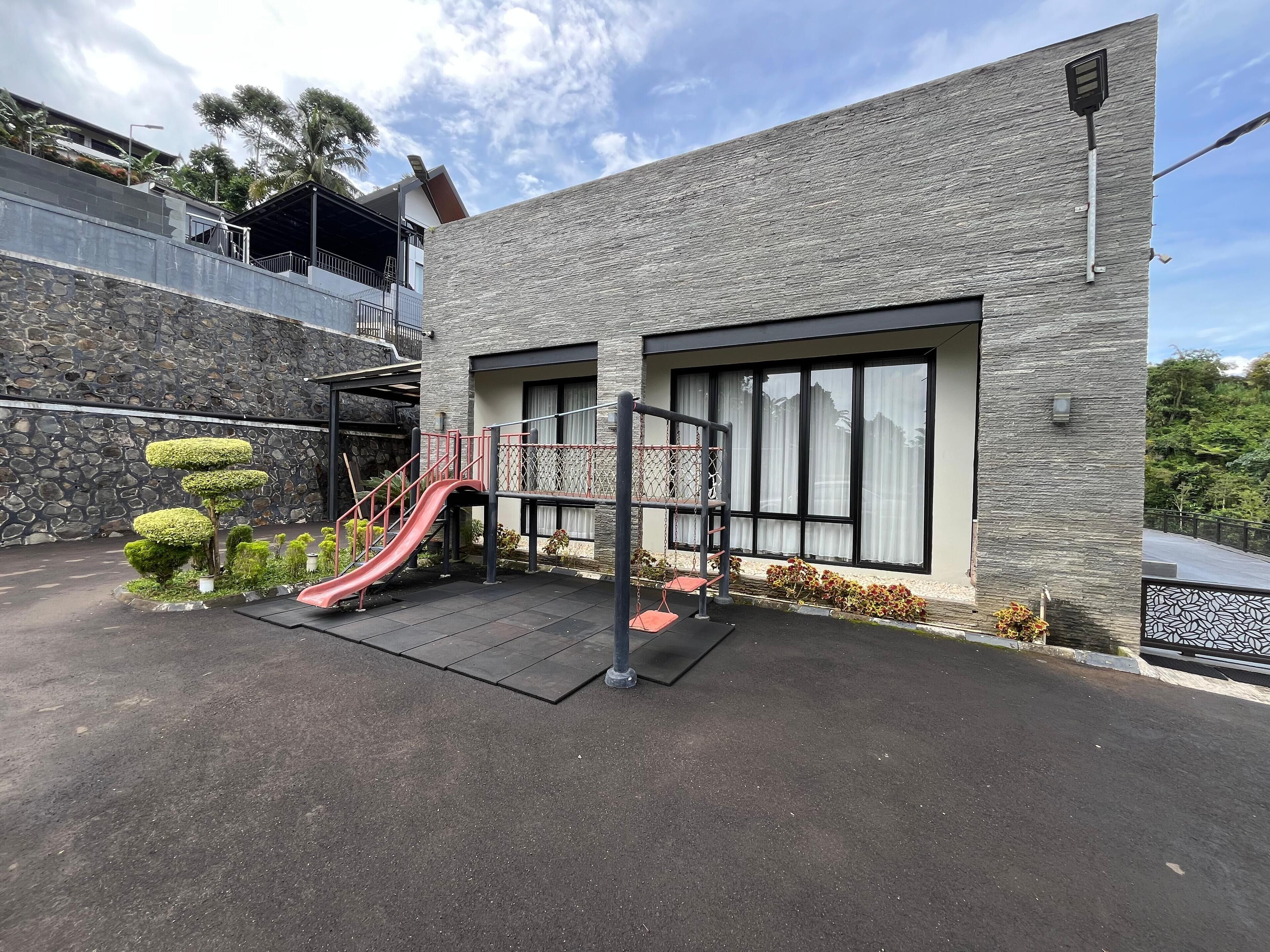 Un edificio moderno con fachada de piedra, amplias ventanas y un área de juegos con un tobogán.