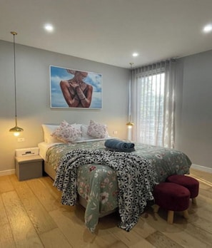 Une chambre à coucher avec un lit, des lampes de chevet, une table de nuit, une fenêtre avec des rideaux et un tableau au mur.