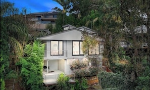 A two-story house with a balcony, surrounded by dense vegetation.