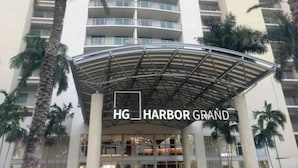 A tall hotel with a curved entrance canopy, palm trees, and the name "HG Harbor Grand" visible. - Harbor View Elite-Luxury Apartment-Amazing Views (Fort Myers)