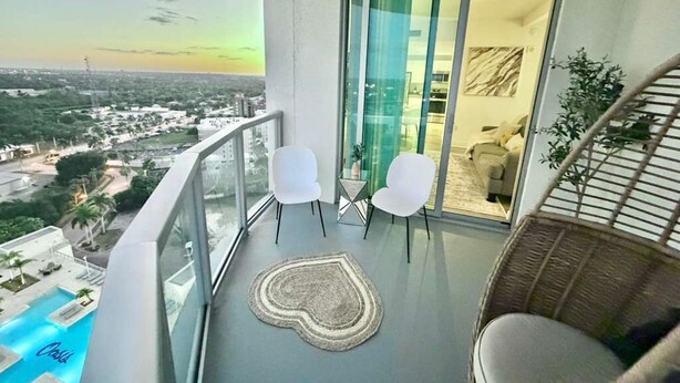 A balcony with a view of a cityscape, a pool, and a wicker chair. - Harbor View Elite-Luxury Apartment-Amazing Views (Fort Myers)