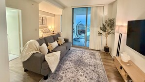 A modern living room with a grey sofa, a large rug, a flat-screen TV, and a balcony with a hanging chair. - Harbor View Elite-Luxury Apartment-Amazing Views (Fort Myers)