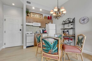 A modern kitchen with wooden cabinets, a white stove, and a microwave. There is a dining area with wicker chairs and a glass table. - Penthouse-Level Retreat | Sweeping Estero Bay Views & Beautiful Sunrises | Resort Pool & Hot Tub (Fort Myers Beach)