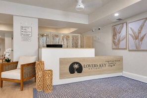 Un espace d’accueil comprenant un comptoir de réception en bois, une chaise, un panneau mural indiquant les directions et des œuvres d’art décoratives.