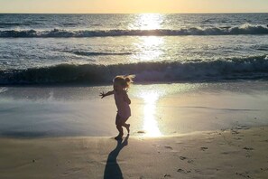 Un enfant joue sur une plage, les vagues déferlent et le soleil brille.