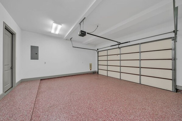 A clean, empty garage with a red speckled floor, a closed garage door, and a ceiling-mounted projector.