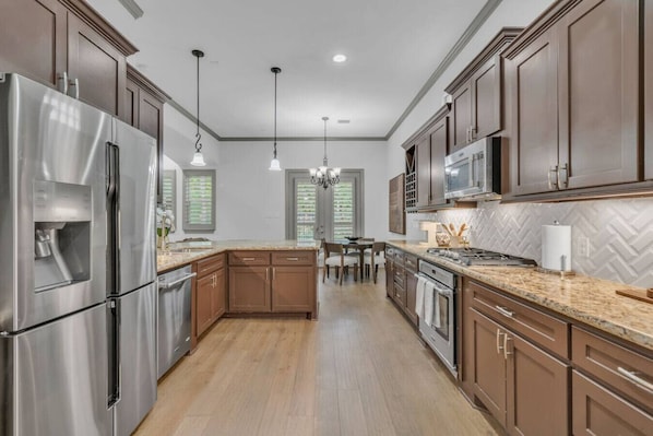 A modern kitchen with stainless steel appliances, wooden cabinets, and a herringbone tile backsplash.