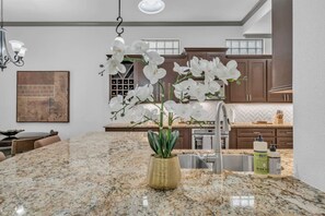 A kitchen with granite countertops, white orchids, a hanging light fixture, and wooden cabinets.
