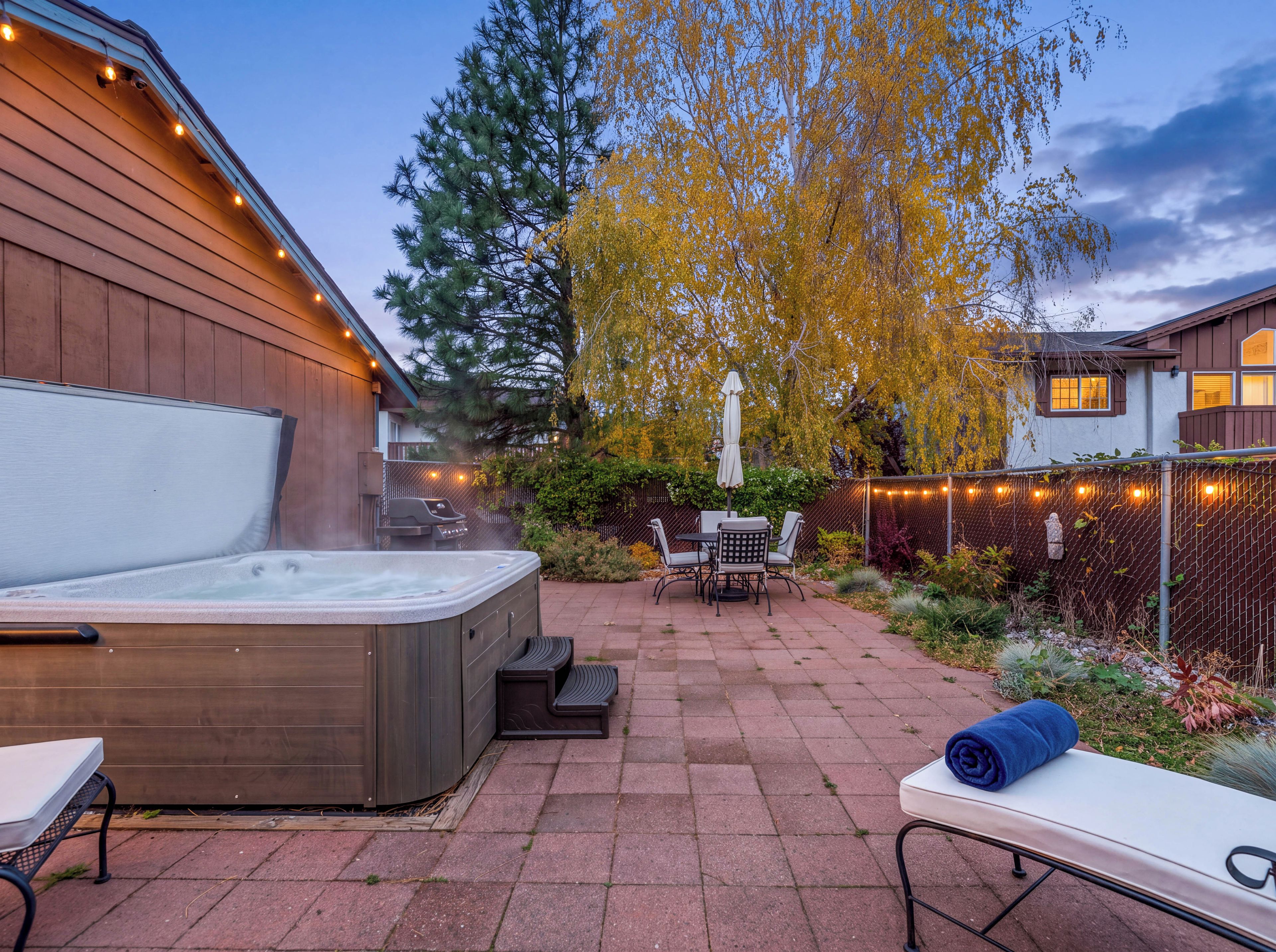 Een hottub, een terras met zitplaatsen en een patio met uitzicht op bomen en een hek.