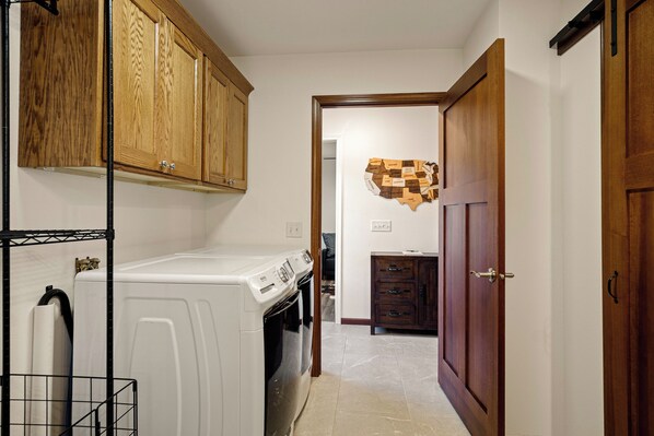 A laundry room with a washing machine and dryer, wooden cabinets, and a map of the USA on the wall. - The RidgeHaus: 40-Acre Farm Stay, Fire Pit & Views (Hixton)