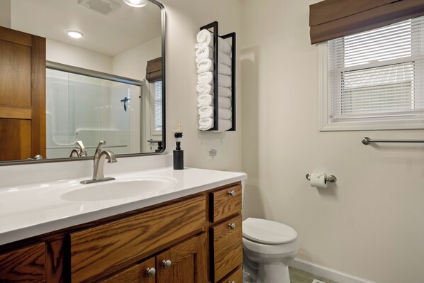 A bathroom with a white sink, wooden vanity, a large mirror, a towel rack, and a toilet.