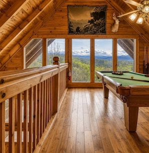Un intérieur en bois avec une table de billard, de grandes fenêtres et un ventilateur de plafond.