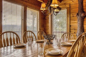 A wooden dining room with a table set for six, surrounded by chairs, and large windows with blinds. - Dolly's View Lodge | Games • Hot Tub • Best Views (Sevierville)