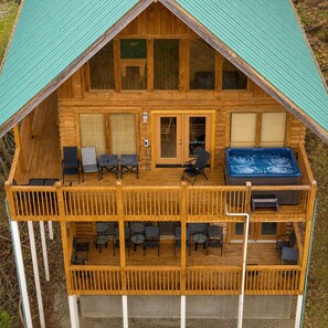 A two-story log cabin with a deck, outdoor seating, and a hot tub. - Dolly's View Lodge | Games • Hot Tub • Best Views (Sevierville)