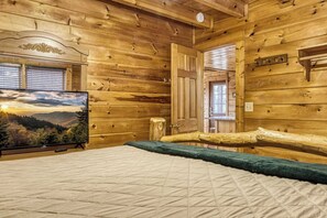 A wooden cabin room with a bed, a television on a stand, and a door leading to another room. - Dolly's View Lodge | Games • Hot Tub • Best Views (Sevierville)