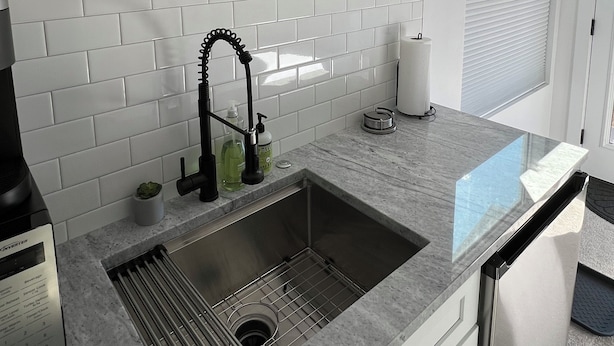 Una cocina moderna con azulejos blancos tipo metro, un lavamanos de acero inoxidable y una planta en el alféizar de la ventana.