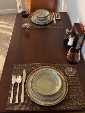 Una mesa de comedor dispuesta con platos, cubiertos y vasos, con salero y pimentero, y un libro a un lado.