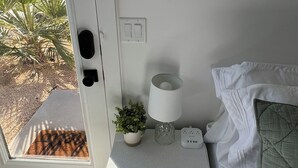 Un dormitorio con cama, una mesita de noche con lámpara, un espejo en la pared y una puerta que da a un jardín.