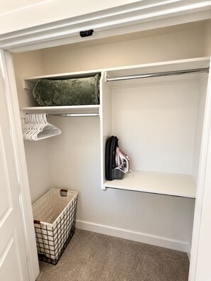 Un vestidor con repisas, espacio para colgar ropa y un contenedor de almacenamiento.